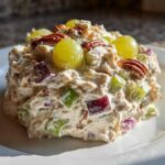 A perfectly molded scoop of The Chicken Salad featuring chicken, celery, red onion, topped with green grapes and pecans.
