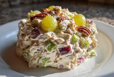 A perfectly molded scoop of The Chicken Salad featuring chicken, celery, red onion, topped with green grapes and pecans.