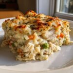 A generous slice of creamy Angel Chicken Rice Casserole showing shredded chicken, rice, peas, carrots, and a golden, cheesy crust.