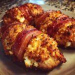 Four pieces of crispy Bacon Wrapped Garlic Parmesan Chicken, cooked until golden brown and served on a dark plate.