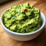 Close-up of chunky, bright green Basic Guacamole topped with cilantro and red pepper flakes in a white bowl.