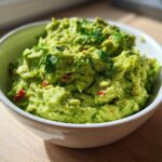 A close-up of chunky, bright green basic guacamole topped with cilantro in a white bowl.
