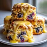 Stack of warm Blueberry Butter Swim Biscuits generously drizzled with thick, bright yellow lemon glaze.