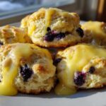A stack of fluffy Blueberry Butter Swim Biscuits generously topped with dripping lemon glaze.