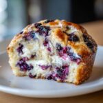 Close-up of a bakery style Blueberry Cream Cheese Muffin Cake cut in half showing swirls of cream cheese and juicy blueberries.