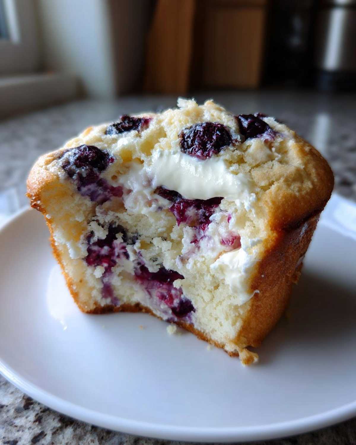 Close-up of a bakery-style Blueberry Cream Cheese Muffin Cake cut in half, showing fluffy cake, cream cheese filling, and blueberries.