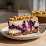 A perfect slice of Blueberry Crumble Cheesecake showing a graham cracker crust, creamy filling, and vibrant blueberry swirls.
