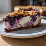 A close-up of a perfect slice of Blueberry Crumble Cheesecake with a graham cracker crust and crumb topping.