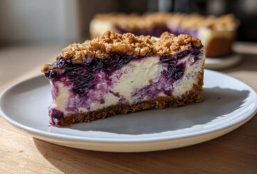 A close-up of a perfect slice of Blueberry Crumble Cheesecake with a graham cracker crust and crumb topping.