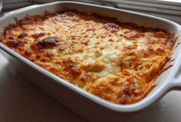 A close-up of hot, bubbly Buffalo Chicken Dip with a perfectly browned and melted cheese topping in a white baking dish.
