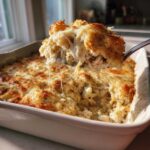 A spoonful of cheesy, shredded Chicken Cauliflower Rice Casserole being lifted from a white baking dish.