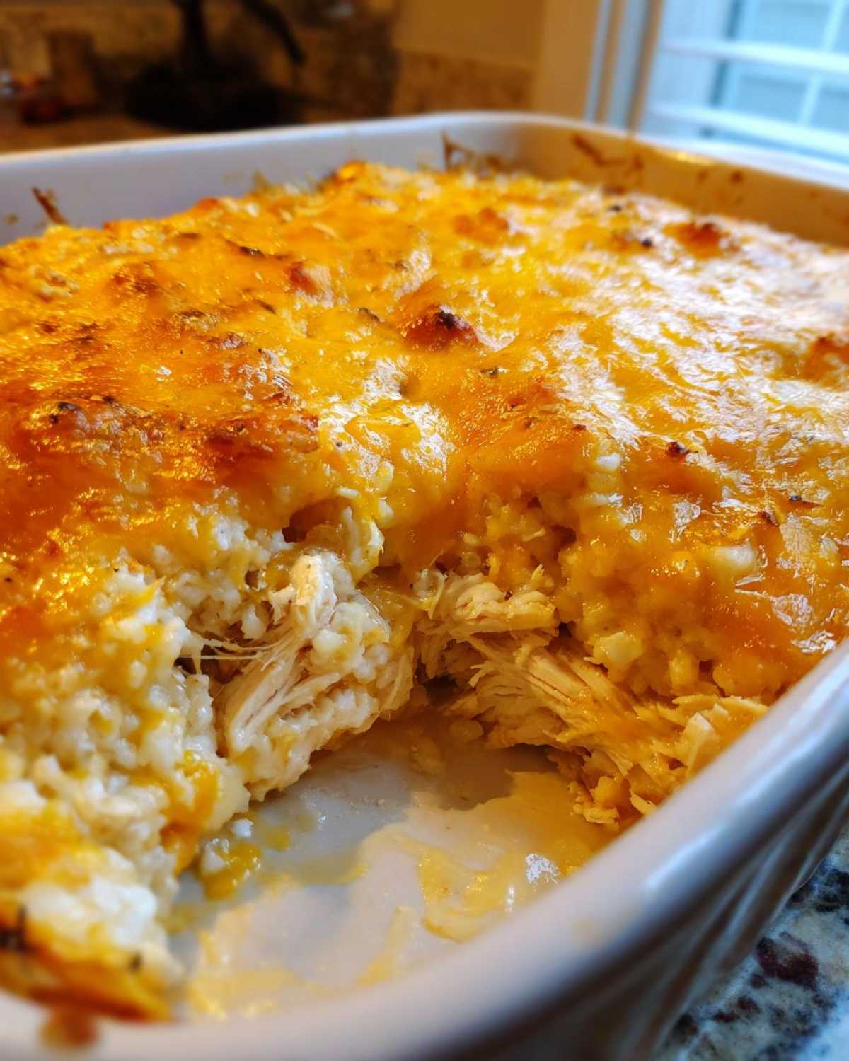 Close-up of a baked Chicken Cauliflower Rice Casserole with a scoop taken out, revealing shredded chicken and a melted cheddar cheese topping.