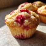 A close-up, sunlit view of one of the delicious Cottage Cheese Strawberry Muffins with bright red fruit visible on top.