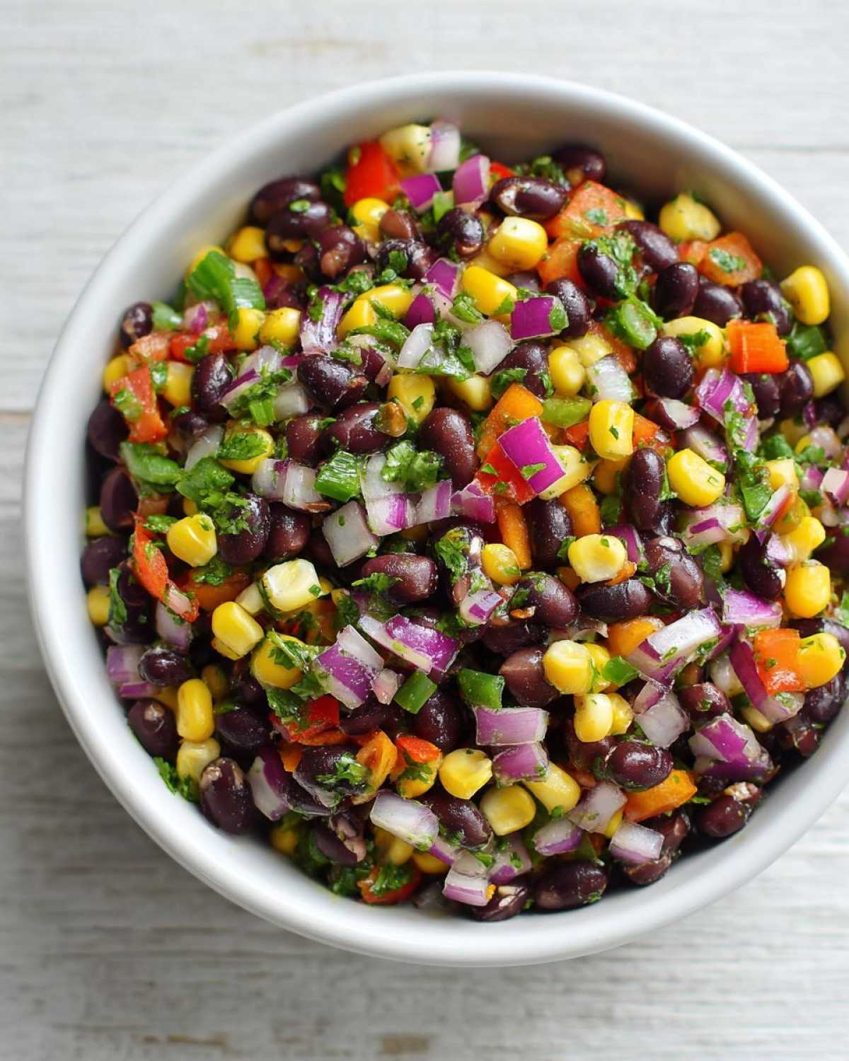 Close-up overhead view of Cowboy Caviar Dip featuring black beans, corn, red onion, and peppers in a white bowl.