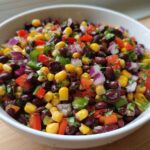 Close-up of vibrant Cowboy Caviar Dip featuring black beans, corn, red onion, and peppers in a white bowl.