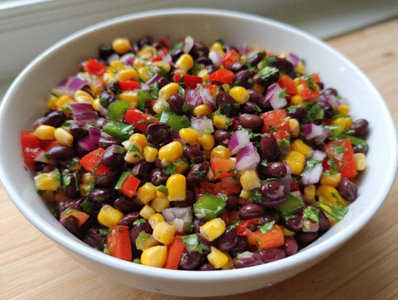 Close-up of vibrant Cowboy Caviar Dip featuring black beans, corn, red onion, and peppers in a white bowl.