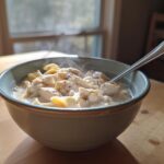 A steaming bowl of creamy Crack Chicken Noodle Soup featuring chunks of chicken and egg noodles, set on a wooden table.