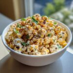 A white bowl filled with creamy Mexican Street Corn Salad, topped with chili powder and cilantro.