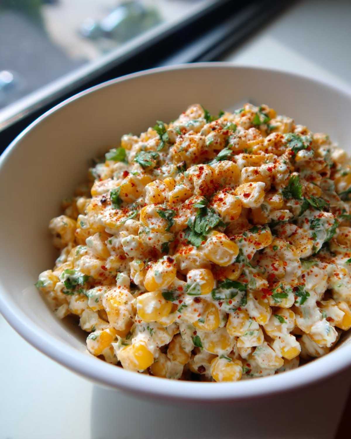 Close-up of Mexican Street Corn Salad mixed with creamy dressing, cilantro, and sprinkled with chili powder.