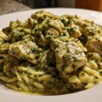 Close-up of tender chicken pieces coated in green pesto sauce served over orzo pasta, a perfect Creamy Pesto Chicken dish.