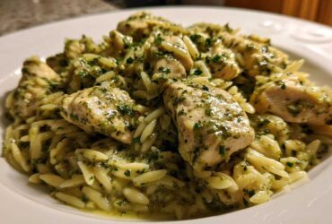 Close-up of tender chicken pieces coated in green pesto sauce served over orzo pasta, a perfect Creamy Pesto Chicken dish.