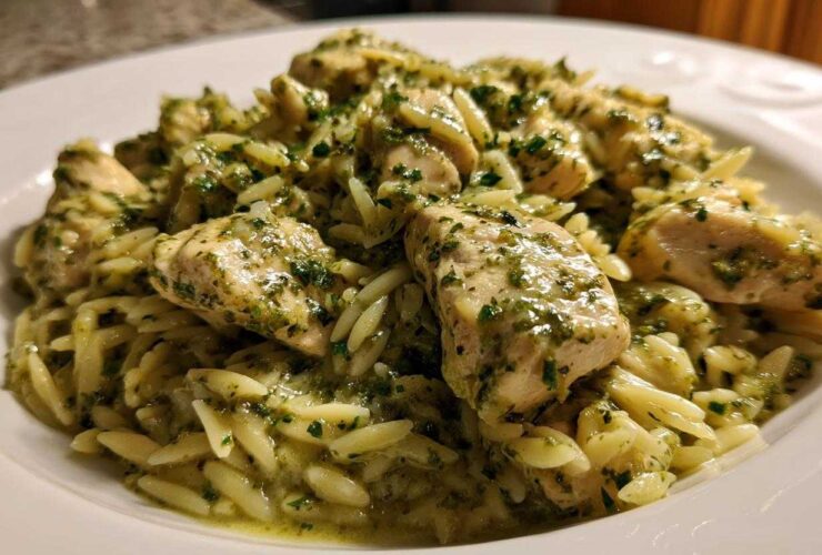 Close-up of tender chicken pieces coated in green pesto sauce served over orzo pasta, a perfect Creamy Pesto Chicken dish.