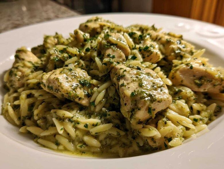 Close-up of tender chicken pieces coated in green pesto sauce served over orzo pasta, a perfect Creamy Pesto Chicken dish.