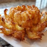 A perfectly cooked, golden brown Crispy Air Fryer Blooming Onion served on a rectangular white plate.