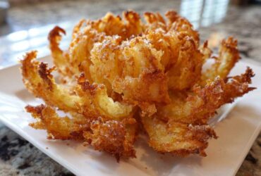 A perfectly cooked, golden brown Crispy Air Fryer Blooming Onion served on a rectangular white plate.