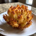 A whole, fully bloomed onion, perfectly cooked and crispy from the air fryer, resting on a white plate.