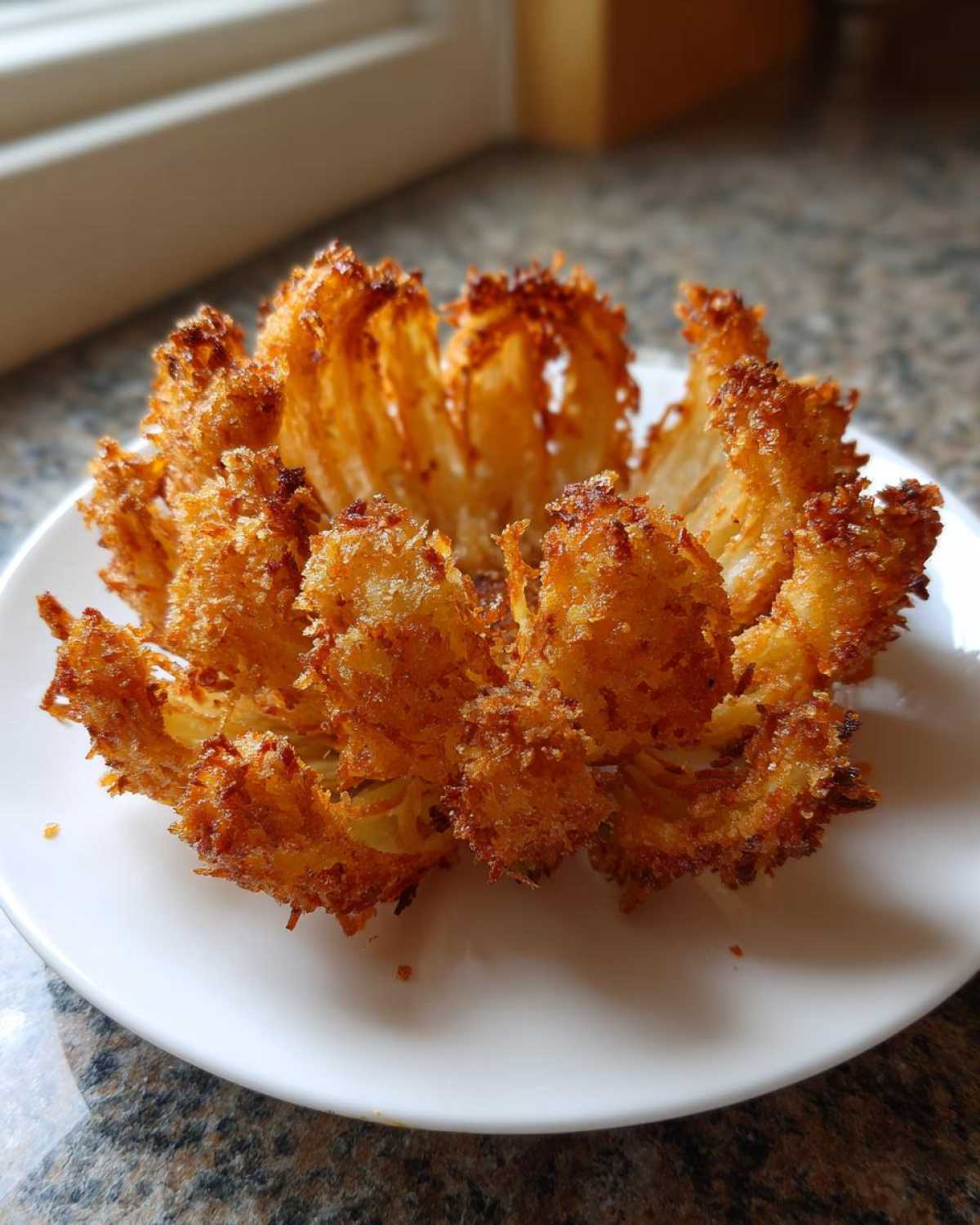 A golden brown, crispy air fryer blooming onion served whole on a white plate.