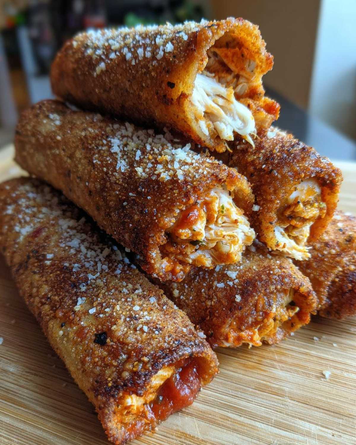 A stack of golden brown, crispy oven rolled chicken taquitos delight, showing shredded chicken filling and a dusting of parmesan cheese.