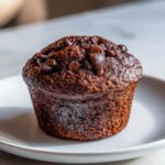 A close-up of a rich, dark Double Chocolate Muffins for Morning Indulgence sitting on a white plate.