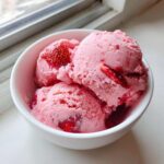 Three scoops of vibrant pink Fresh Strawberry Dream Ice Cream studded with real strawberry pieces in a white bowl.