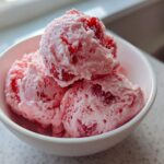 Three scoops of pink Fresh Strawberry Dream Ice Cream, studded with visible strawberry pieces, served in a white bowl.