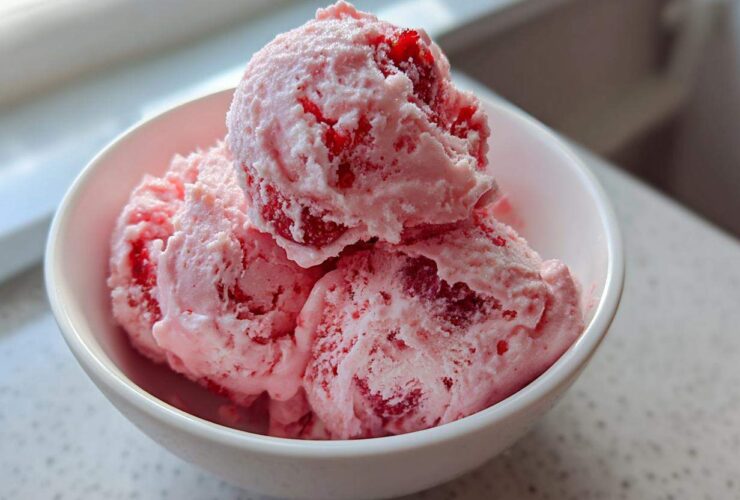 Three scoops of pink Fresh Strawberry Dream Ice Cream, studded with visible strawberry pieces, served in a white bowl.