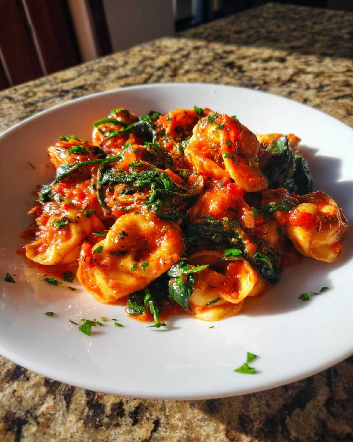 A white bowl filled with Garlic and Herb Tomato Tortellini mixed with wilted spinach and fresh parsley.