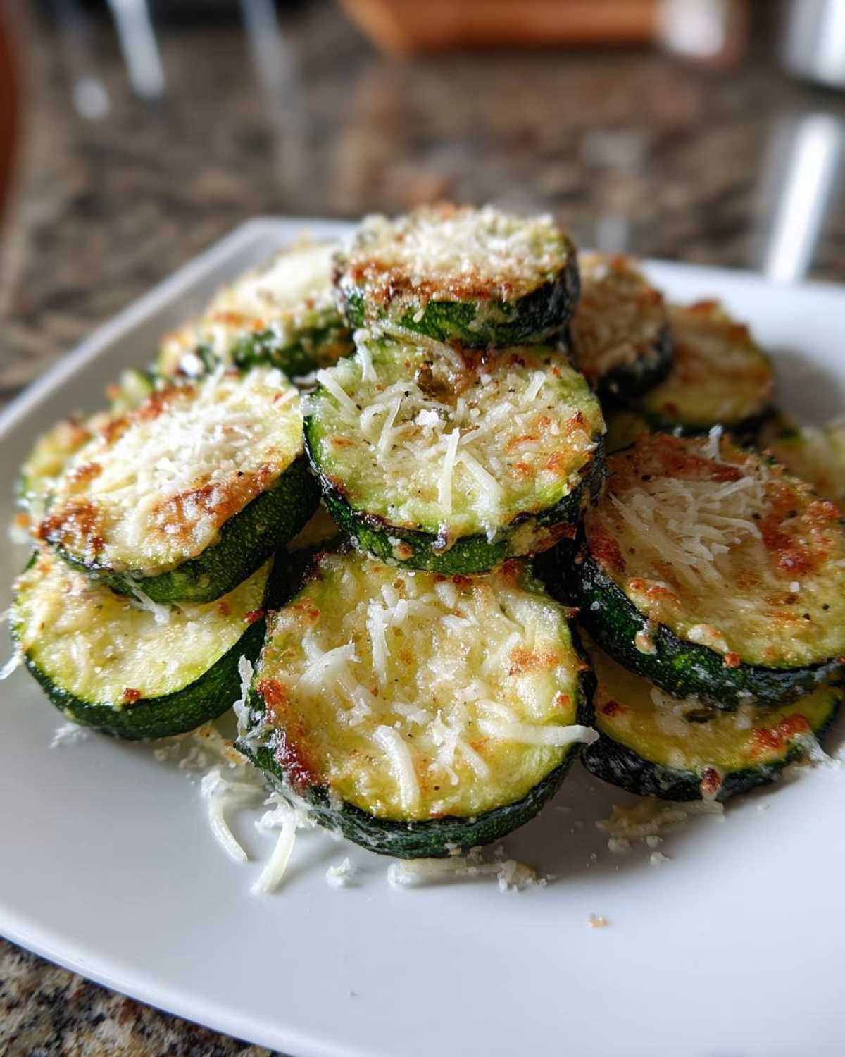 A stack of roasted zucchini slices topped with melted and shredded Parmesan cheese for Garlic Parmesan Zucchini Roast.