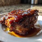 A close-up of a piece of richly glazed Hawaiian Huli Huli Chicken sitting in its sauce on a white plate.