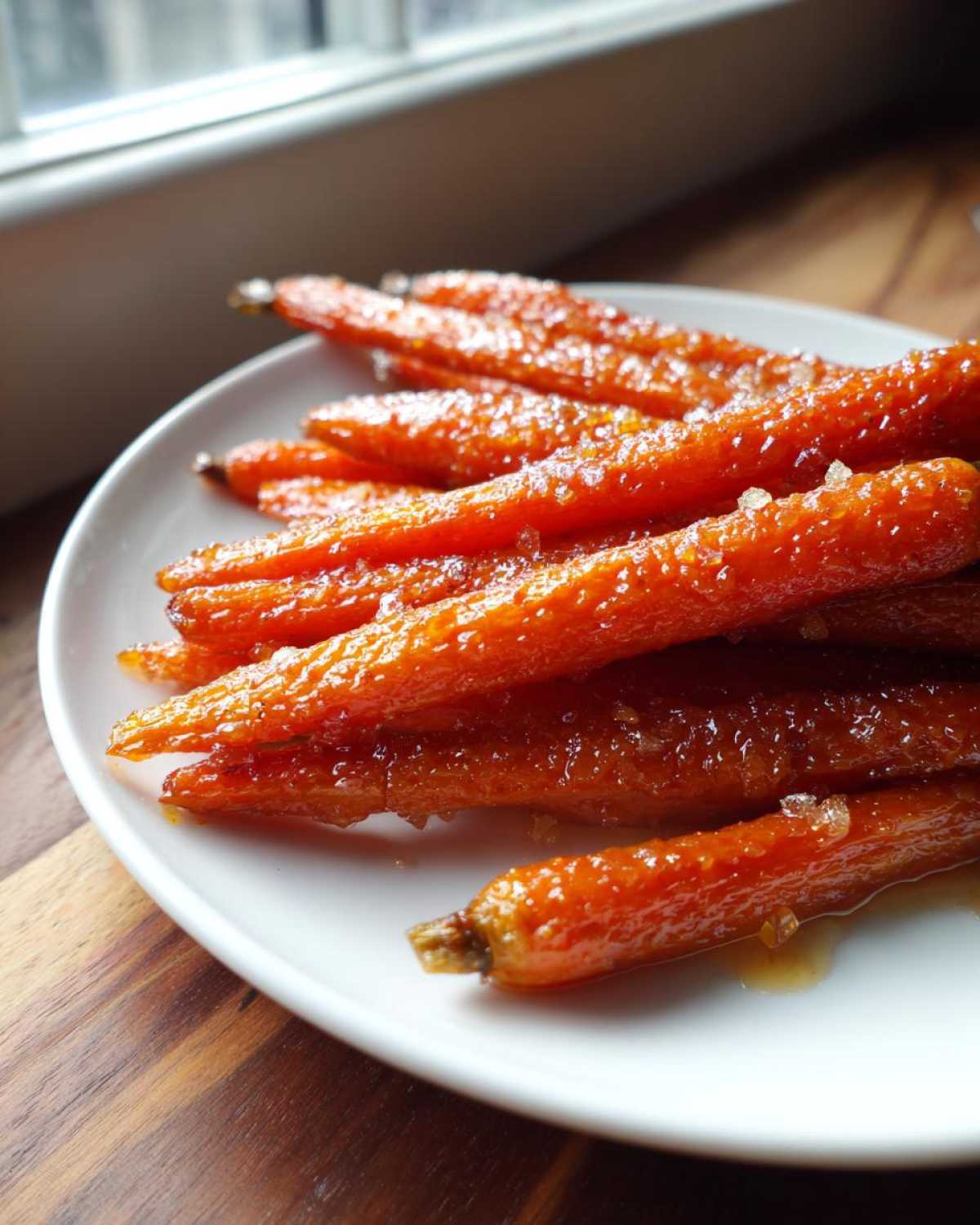 Close-up of Glazed Honey Garlic Butter Roasted Carrots piled on a white plate, glistening with glaze.