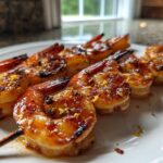 Close-up of perfectly glazed Grilled Honey Garlic Shrimp skewers garnished with lemon zest on a white plate.