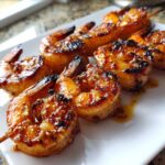 Close-up of succulent Grilled Honey Garlic Shrimp skewers with a caramelized, glossy glaze and sesame seeds on a white plate.
