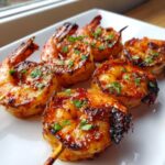 Close-up of perfectly grilled Sweet Chili Bang Bang Shrimp Skewers glazed with sauce and topped with fresh parsley on a white plate.