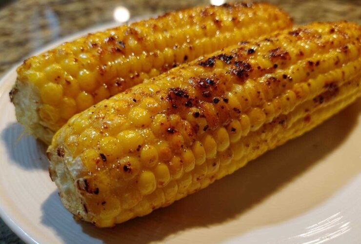 Close-up of two perfectly Grilled Sweet Corn on the Cob cobs glistening on a white plate with visible char marks.