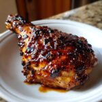 A close-up of a juicy chicken drumstick coated in a thick, dark, caramelized glaze, characteristic of Hawaiian Huli Huli Chicken.