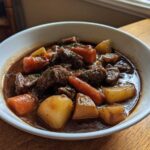 A close-up of a white bowl filled with rich, dark Irish Veggie Stew featuring chunks of beef, carrots, and potatoes.