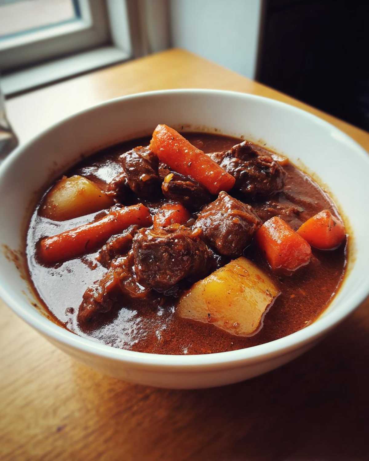 Close-up of a rich, dark brown bowl of Irish Veggie Stew featuring chunks of beef, bright orange carrots, and yellow potatoes.