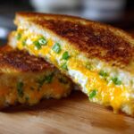 Close-up of a Jalapeño Popper Grilled Cheese Sandwich cut in half, showing gooey melted cheese and green jalapeño pieces.