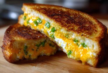 Close-up of a Jalapeño Popper Grilled Cheese Sandwich cut in half, showing gooey melted cheese and green jalapeño pieces.