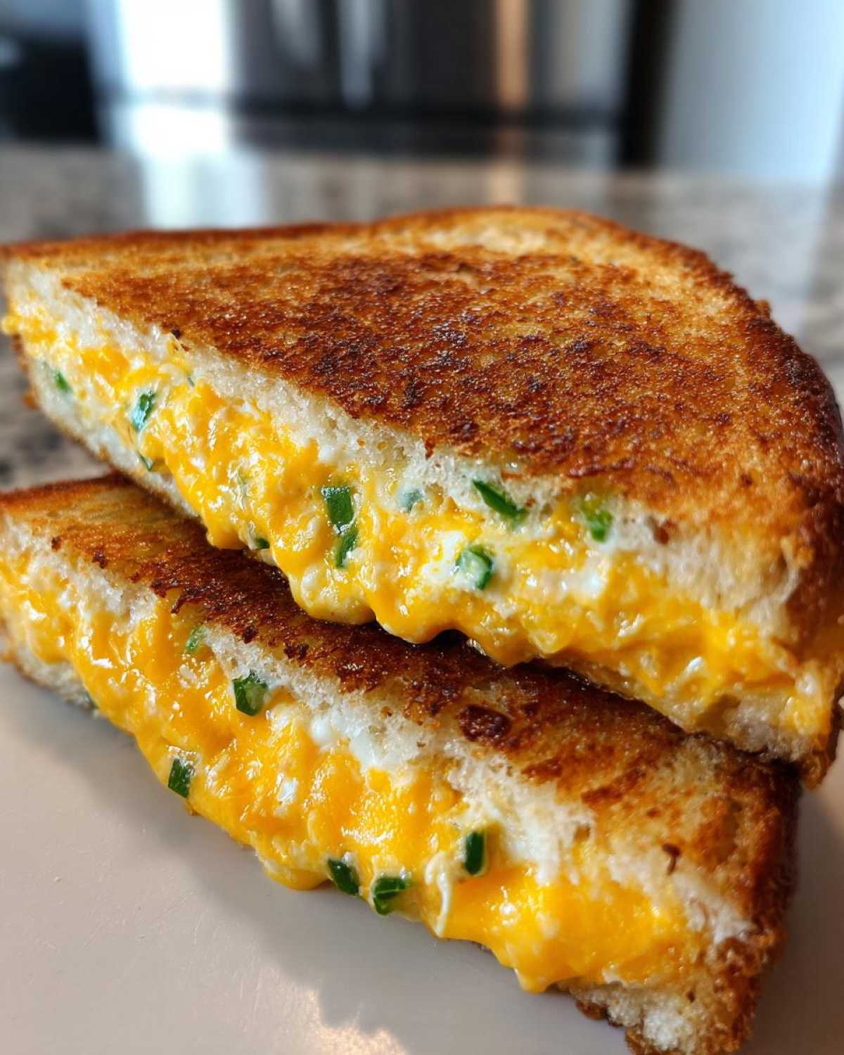 Close-up of a Jalapeño Popper Grilled Cheese Sandwich cut in half, showing gooey orange cheese and green peppers.